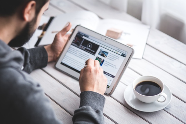 Mann surft auf Tablet mit Kaffee