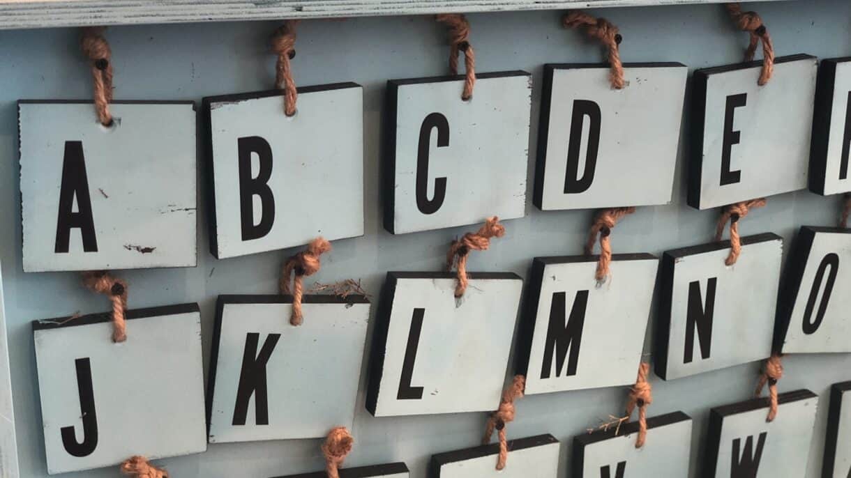 Buchstabentafel aus Holz mit Seilhängern.