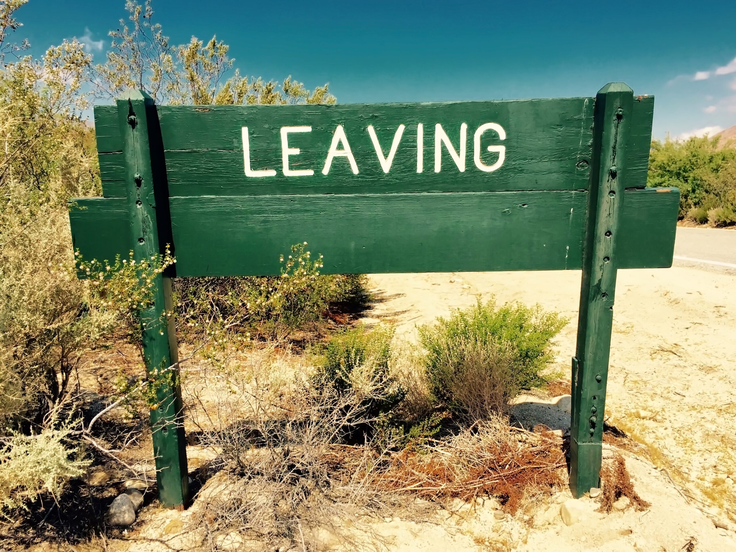 Grünes Schild mit 'LEAVING' im Wüstenhintergrund.