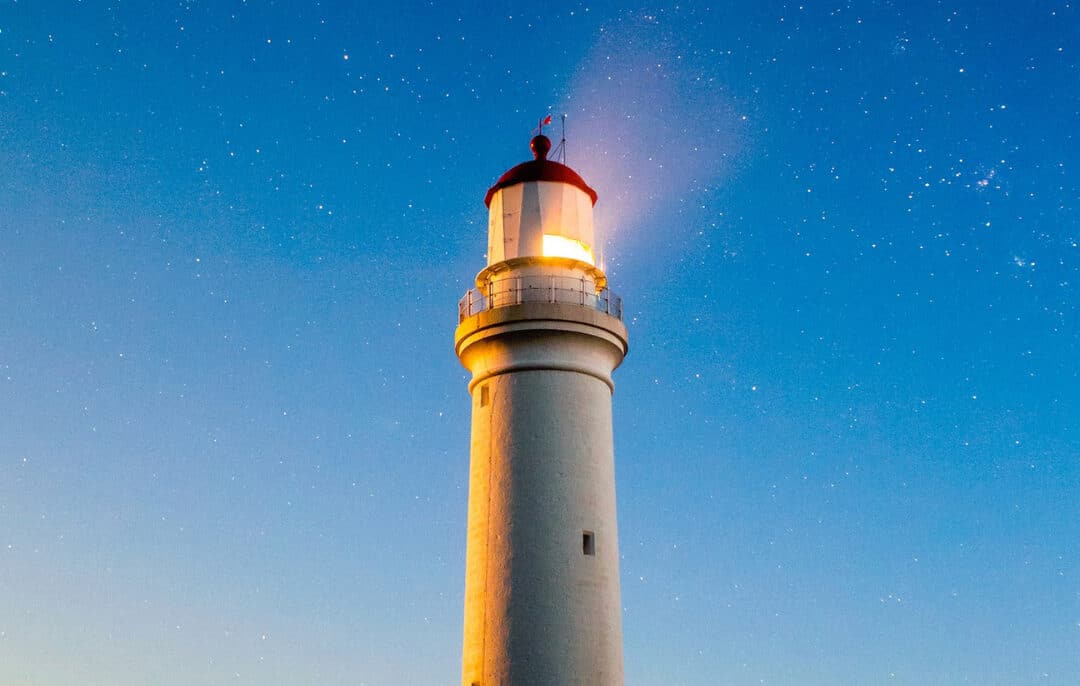 Leuchtturm leuchtet nachts unter Sternenhimmel.
