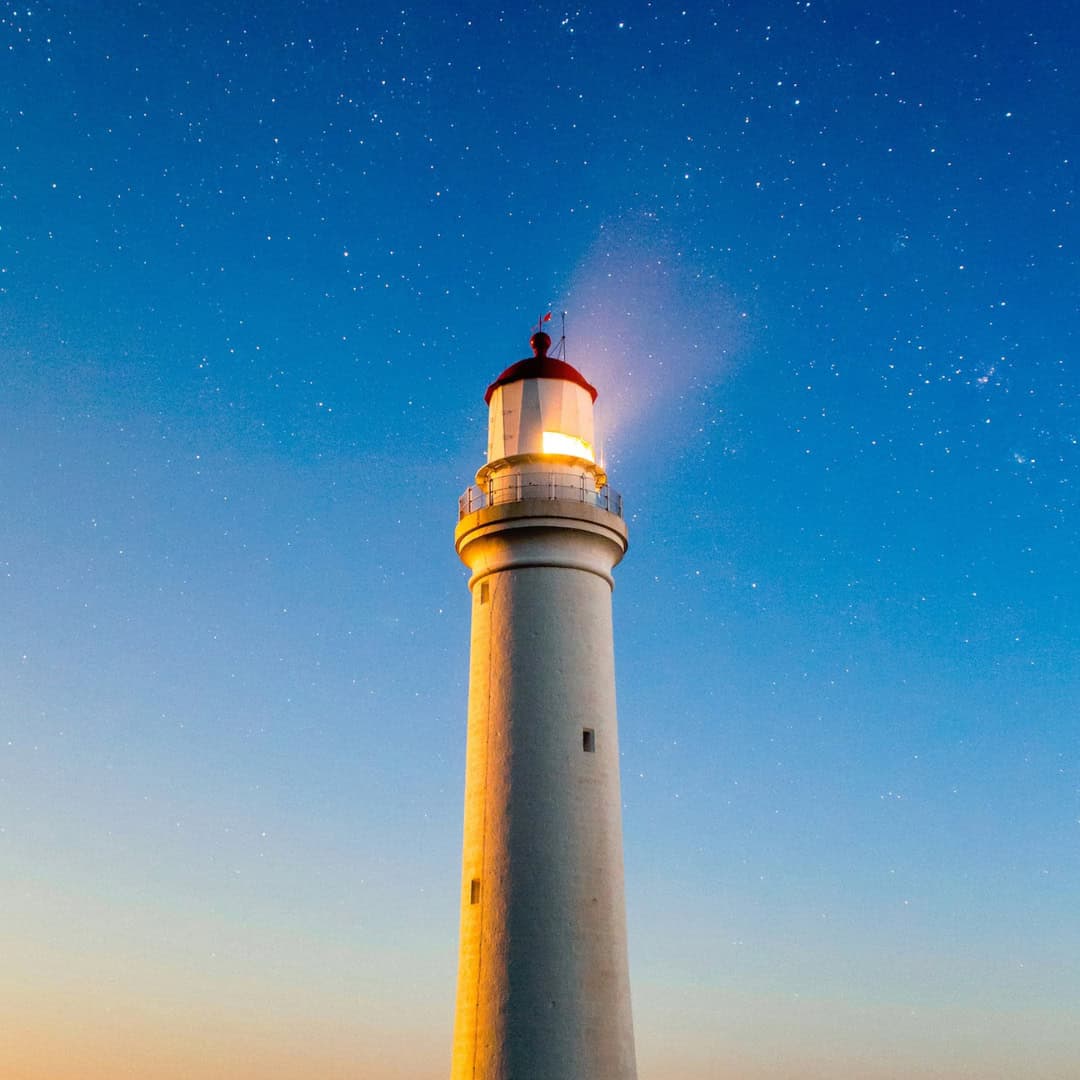 Leuchtturm leuchtet nachts unter Sternenhimmel.